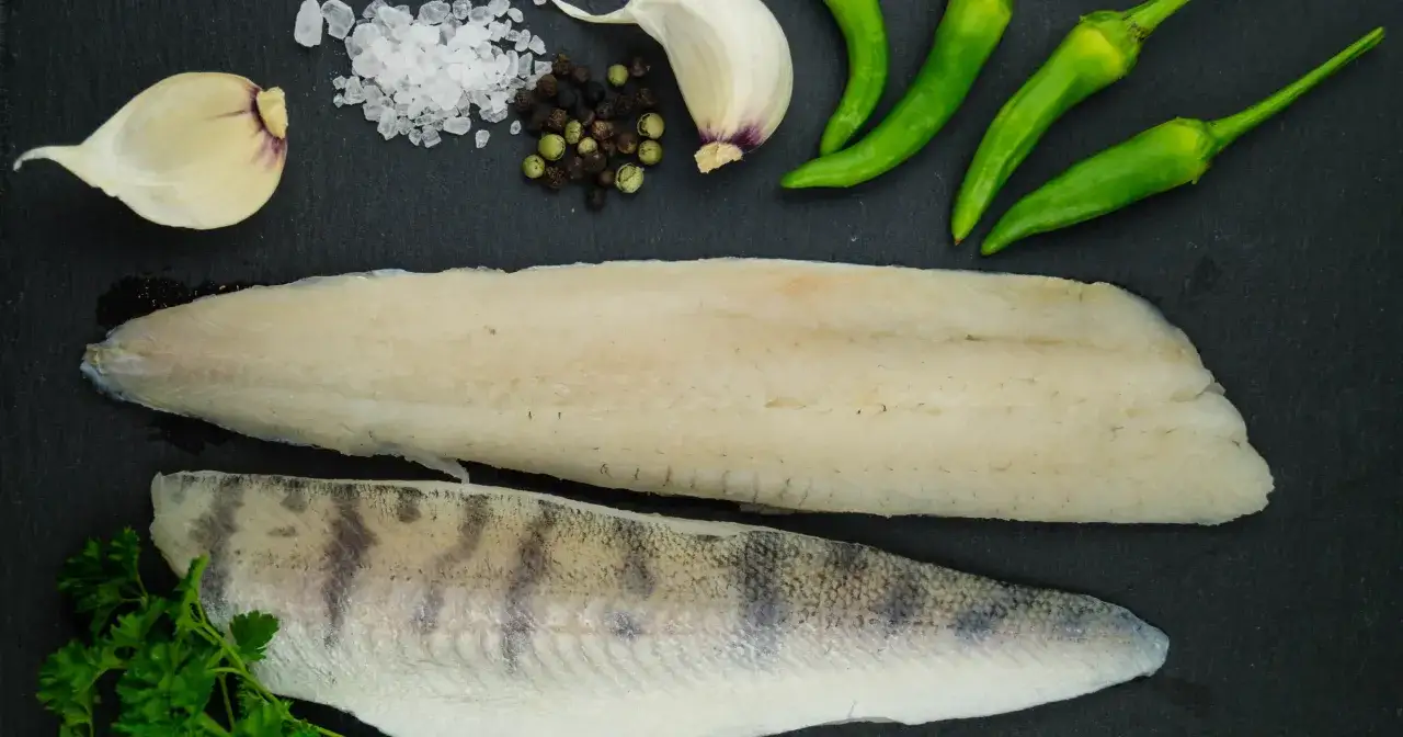 Dwa filety rybne, jeden gładki, drugi z łuską, obok czosnku, pieprzu, soli i papryczek chili. Czy to halibut czy sandacz?