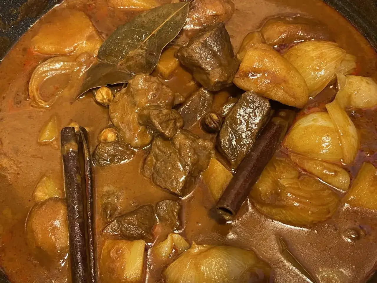 Aromatyczny massaman curry przepis w garnku: kawałki wołowiny, ziemniaki, cebula, laska cynamonu i liść laurowy w gęstym sosie.