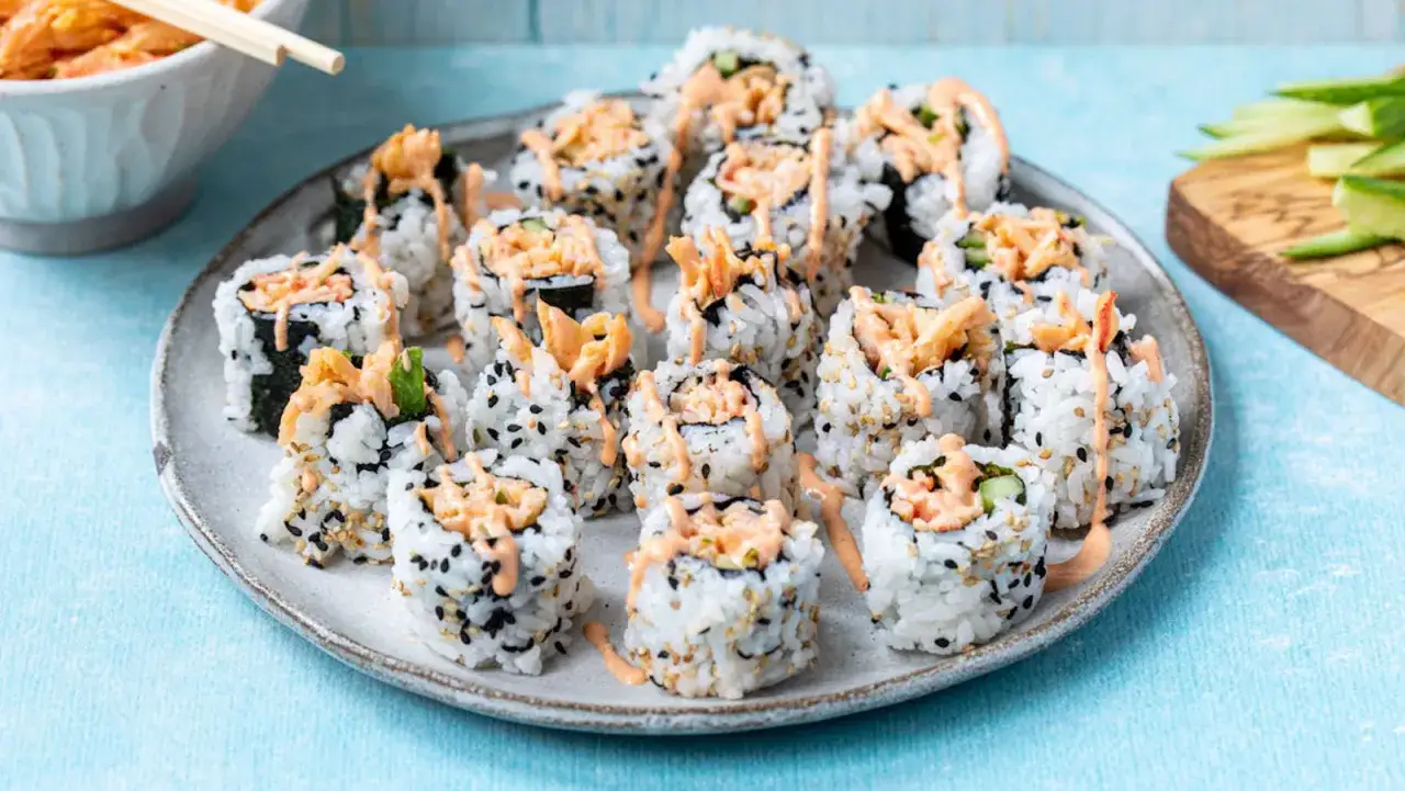 Roladki sushi z paluszkami surimi, ryżem i sezamem, polane pikantnym sosem. Idealne, gdy zastanawiasz się, jak przygotować paluszki surimi do sushi.