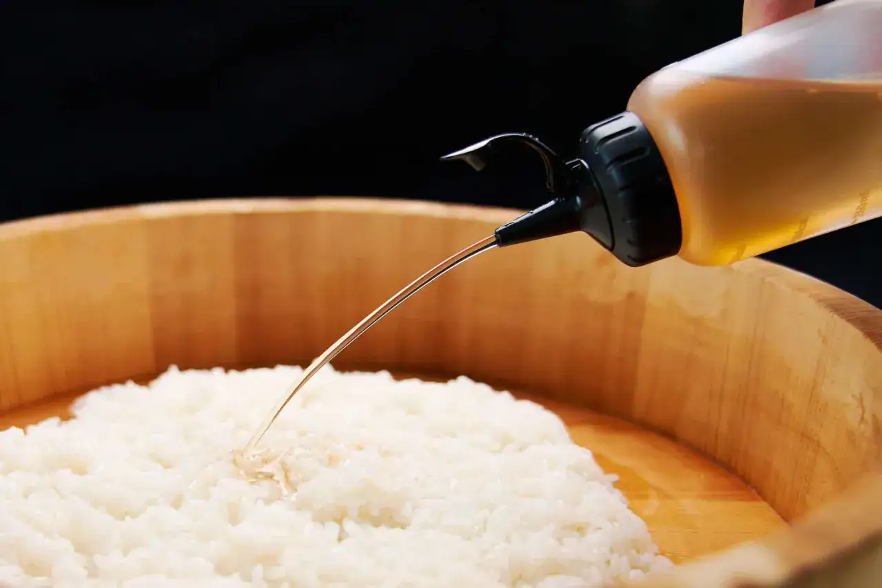 Przygotowanie zaprawy do sushi: płynny sos jest dodawany do ryżu w drewnianej misce.