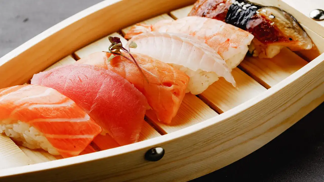 Pięć kawałków sushi z łososiem, tuńczykiem, krewetką i węgorzem w drewnianej łódce. Sushi, które pochodzi z Japonii, zachwyca smakiem.