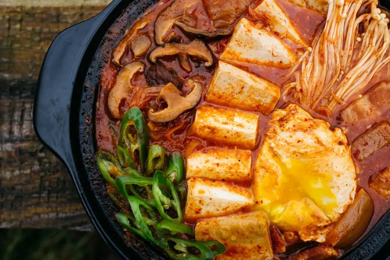 Gorąca zupa z kimchi z tofu, grzybami shiitake, enoki i jajkiem sadzonym. Aromatyczne danie, które rozgrzewa od środka.
