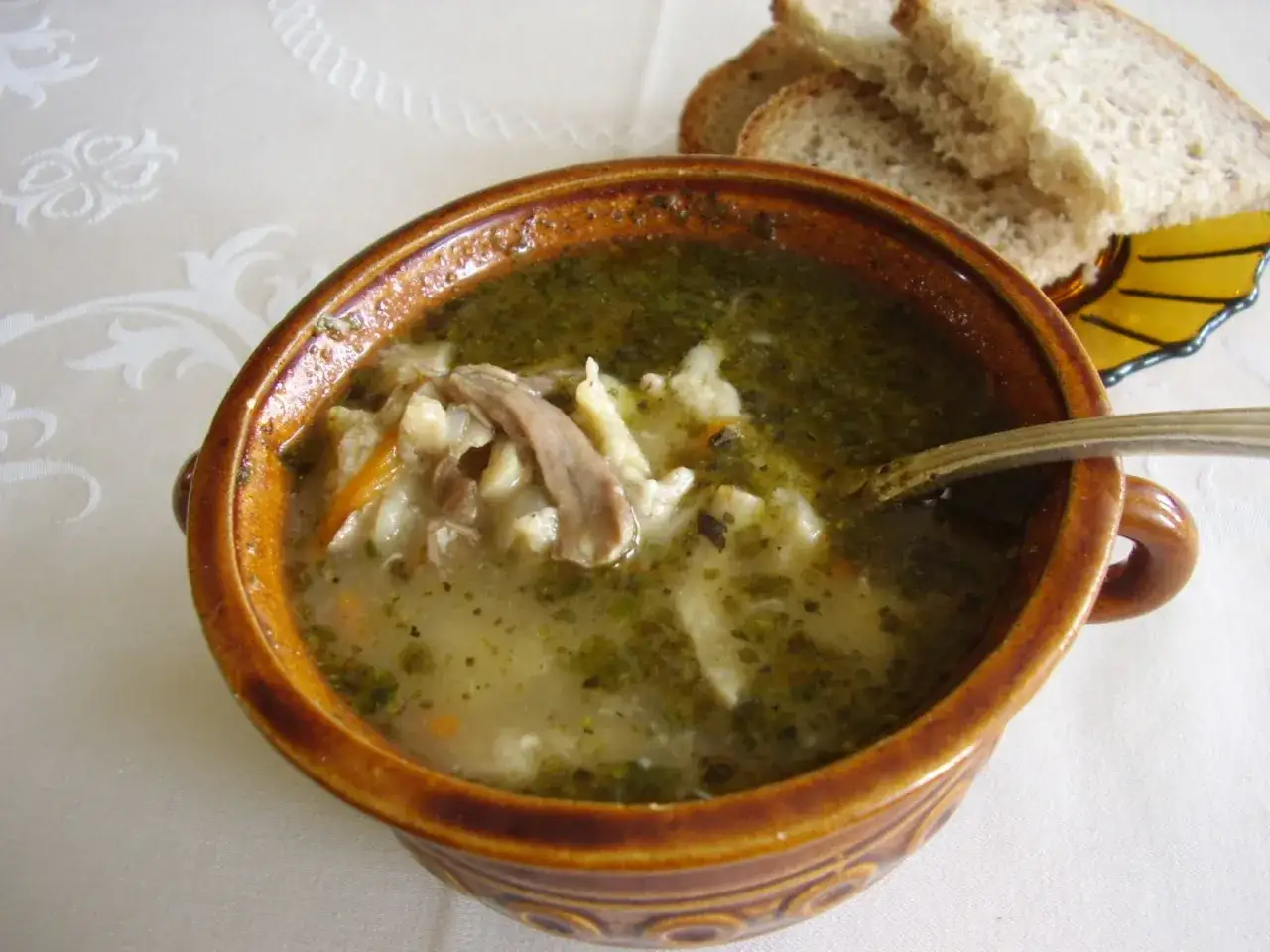 Aromaticzne flaki w glinianej misce, z kawałkami mięsa i warzyw. Obok kromki chleba. Idealne, by dowiedzieć się, jak doprawić flaki.