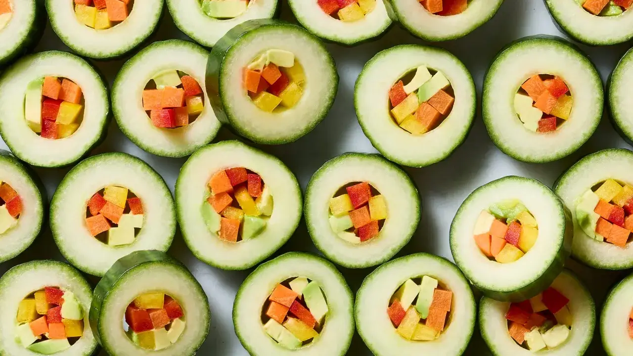 Jak pokroić ogórka do sushi? Krążki ogórka wypełnione kolorowymi warzywami: marchewką, papryką i awokado.