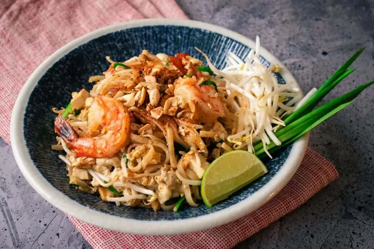 Pyszne danie z makaronem pad thai z krewetkami, kiełkami fasoli mung, orzeszkami ziemnymi i limonką.