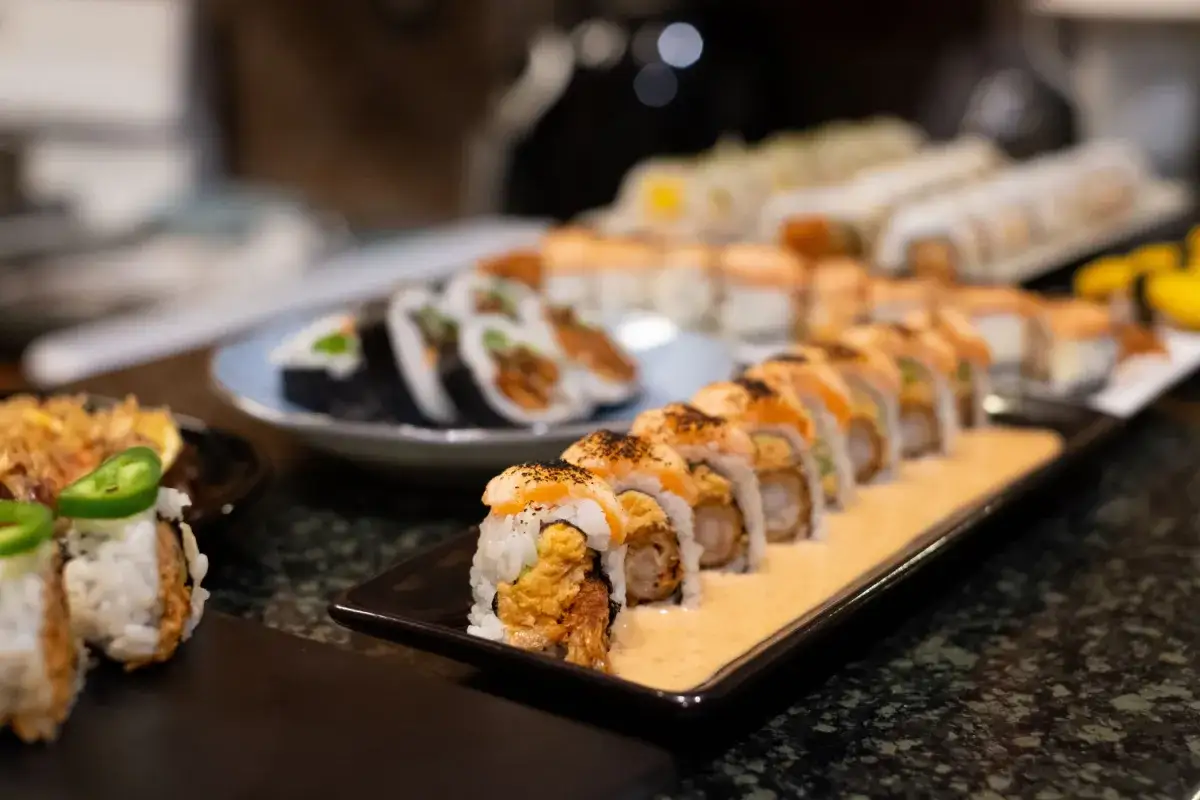 Rząd pysznych hosomak i futomak na czarnym talerzu, z innymi rolkami sushi w tle.
