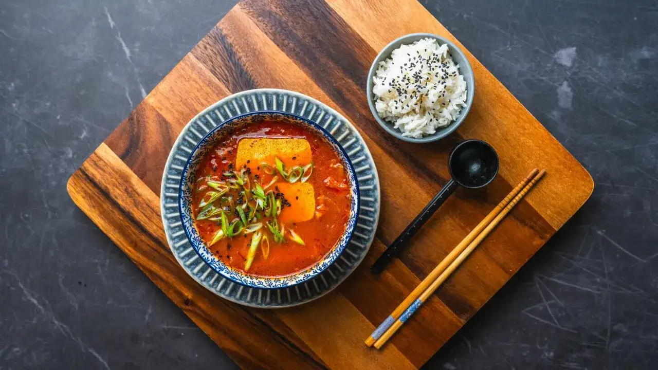 Aksamitna zupa z kimchi z tofu i szczypiorkiem, podana z ryżem i pałeczkami.