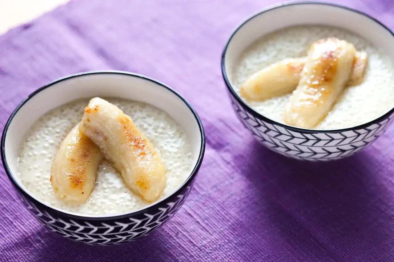 Dwa miseczki z deserem z tapioki na mleku kokosowym, ozdobione karmelizowanymi kawałkami banana.