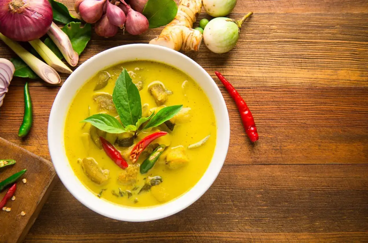 Aromaticzne curry z tofu, ozdobione świeżą bazylią i papryczkami chili, otoczone składnikami: cebulą, trawą cytrynową, imbirem i bakłażanem.