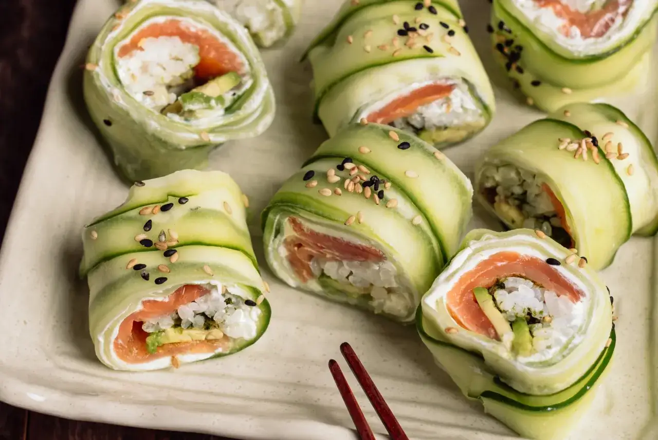 Roladki sushi z łososiem i awokado, zawinięte w cienkie plastry ogórka. Jak pokroić ogórka do sushi? Tak, by wyglądał apetycznie! Posypane sezamem.