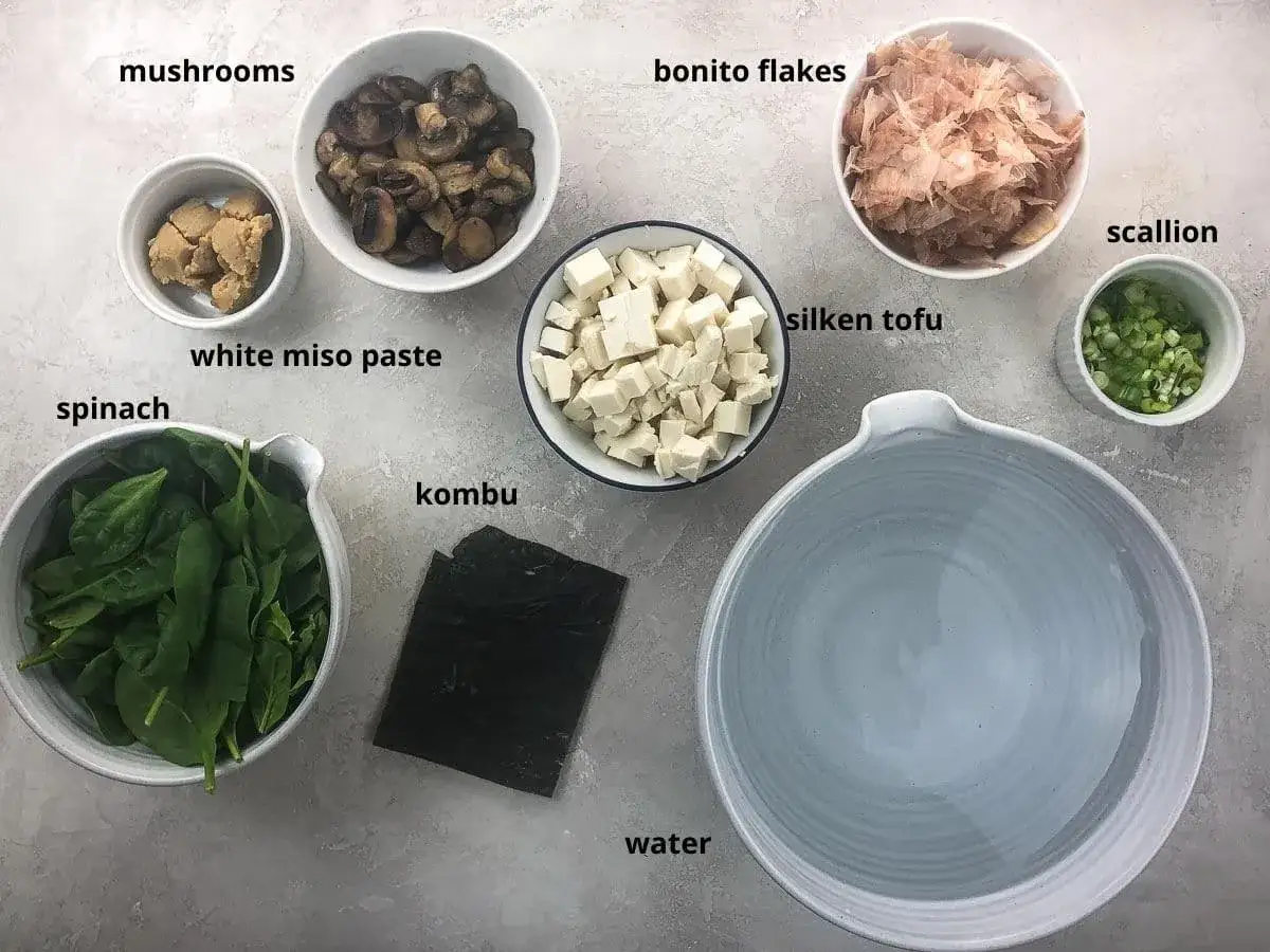 Składniki na zupę miso: tofu, szpinak, grzyby, pasta miso, wodorosty kombu, płatki bonito, szczypiorek i woda.