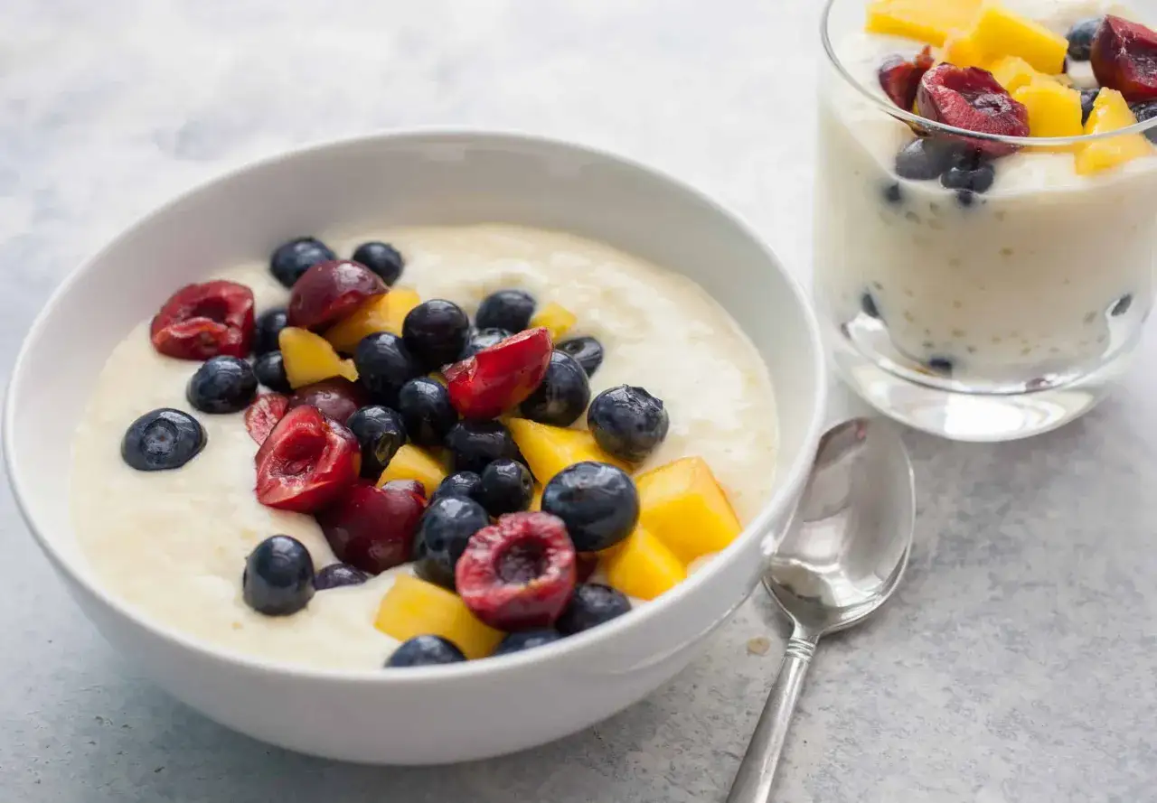 Pudding z tapioki w misce, ozdobiony jagodami, wiśniami i mango. Obok szklanka z tym samym deserem.