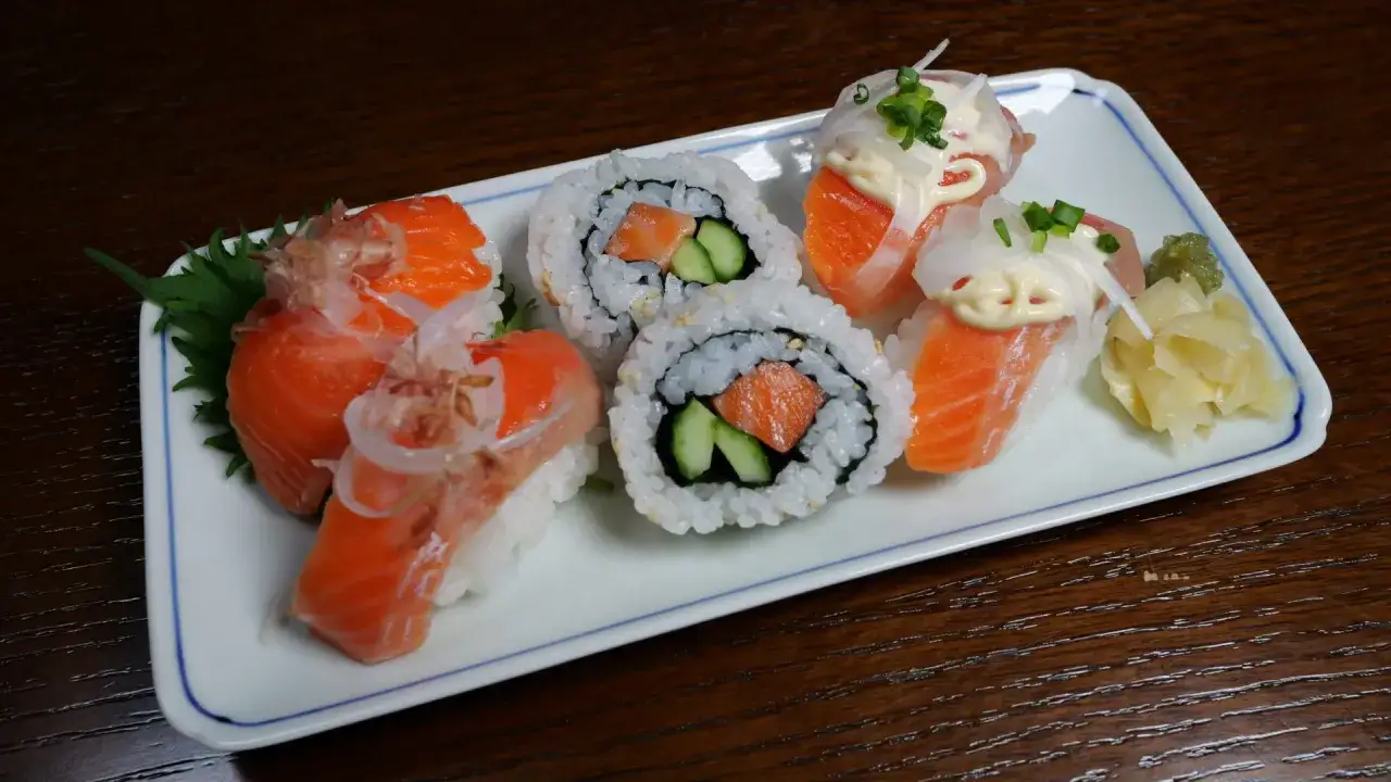 Jak przygotować łososia do sushi? Na talerzu sushi z łososiem, ogórkiem i dodatkami.