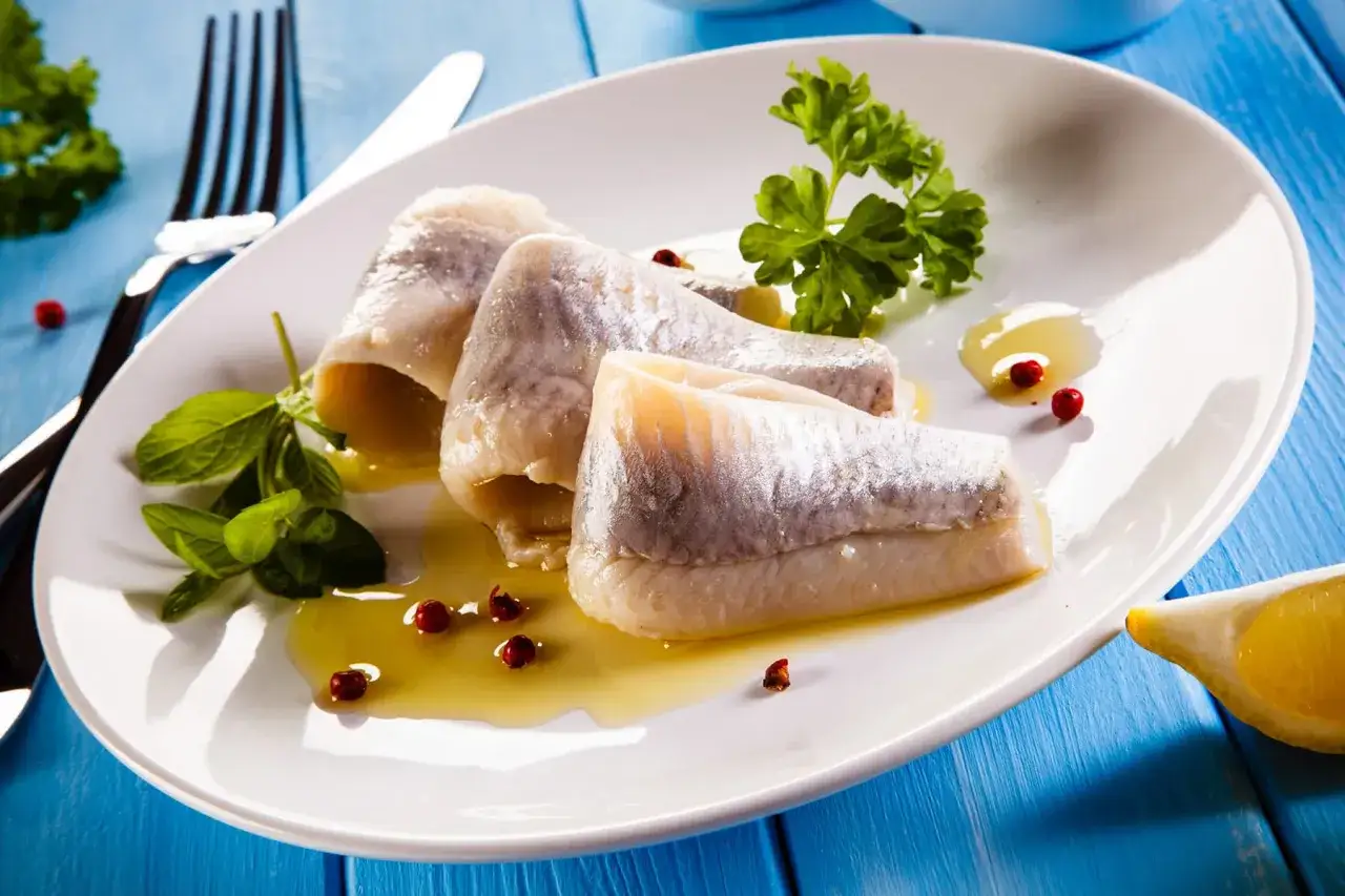 Roladki ze śledzia na talerzu, z cytryną i ziołami. Kto nie powinien jeść śledzi? Alergicy i osoby z problemami z cholesterolem.