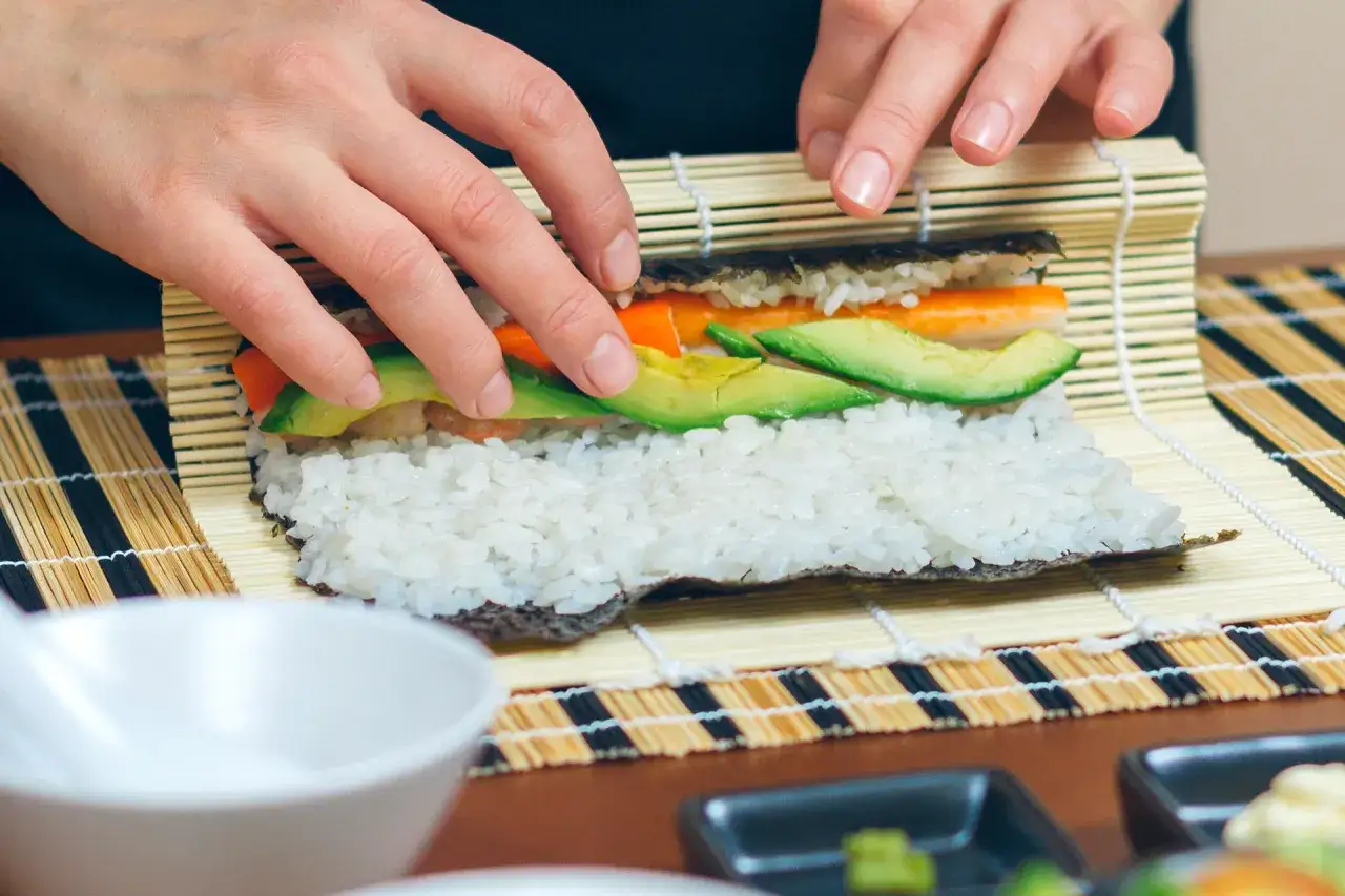 Ręce zwijają sushi z ryżem, awokado i marchewką. Poznaj różne rodzaje sushi i przepisy na domowe rolki.