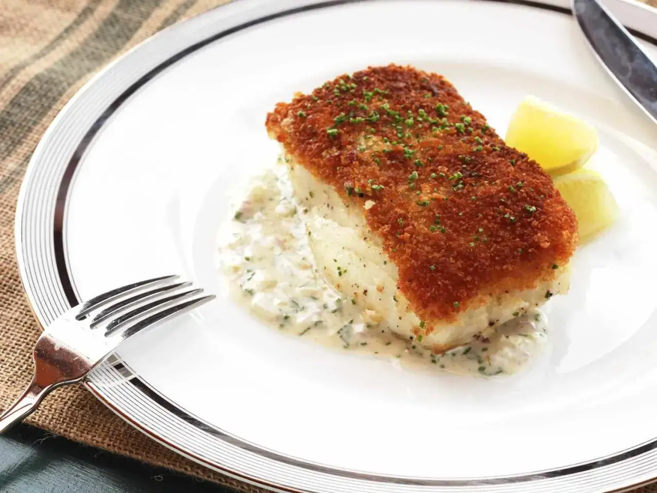 Chrupiący filet z dorsza w panierce, podany z kremowym sosem i cytryną. Idealny przykład, jak usmażyć dorsza na złoto.
