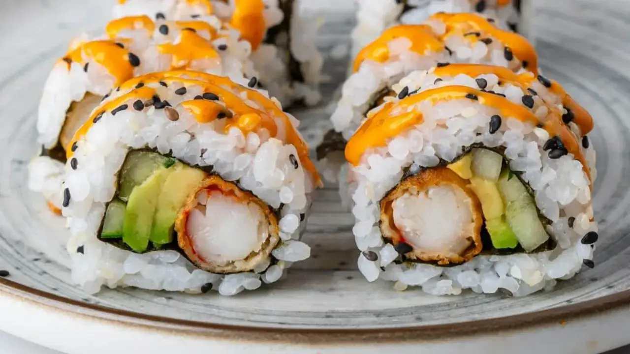 Pyszne sushi z krewetkami w tempurze, awokado i ogórkiem, polane pikantnym sosem i posypane czarnym sezamem.