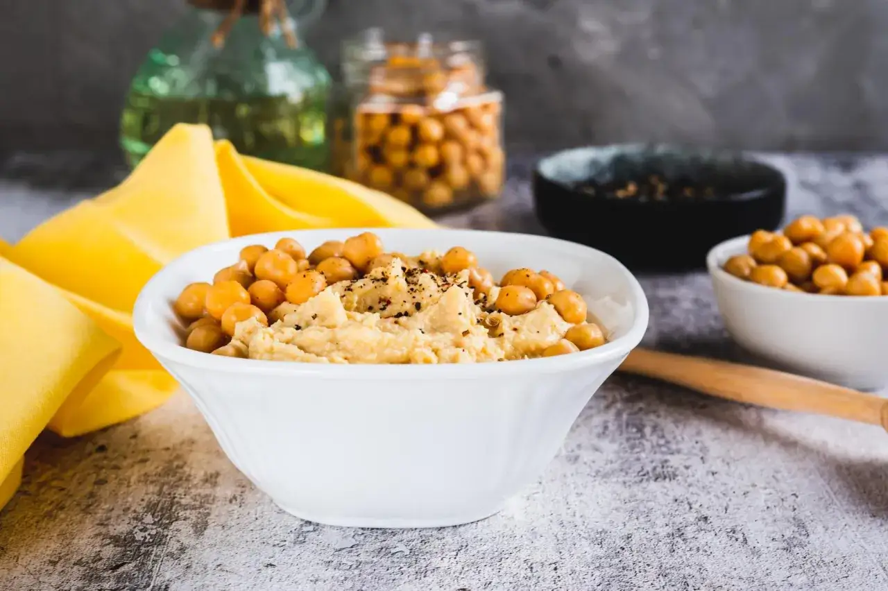 Pyszny hummus z ciecierzycy, posypany ziarnami i podany z żółtym obrusem w tle.