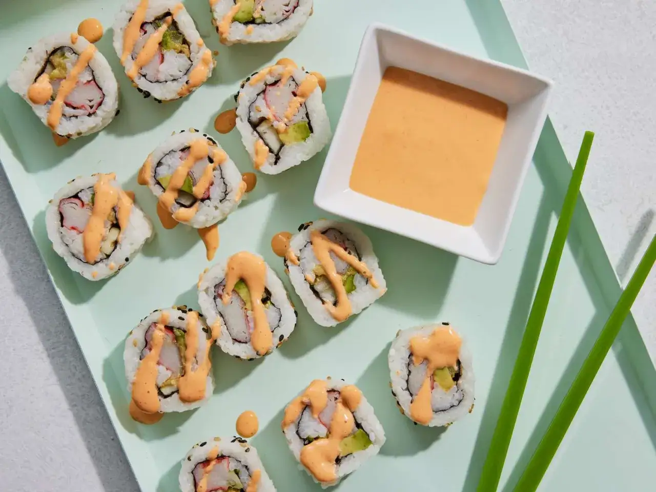 Roladki sushi z awokado i paluszkami krabowymi, polane kremowym sosem majonezowym do sushi.