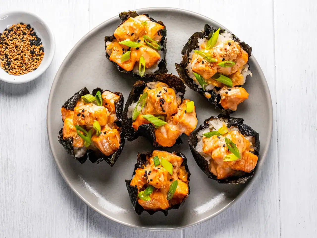 Pięć kuszących miseczek z nori, ryżu i sushi z pieczonym łososiem, posypanych szczypiorkiem i sezamem.