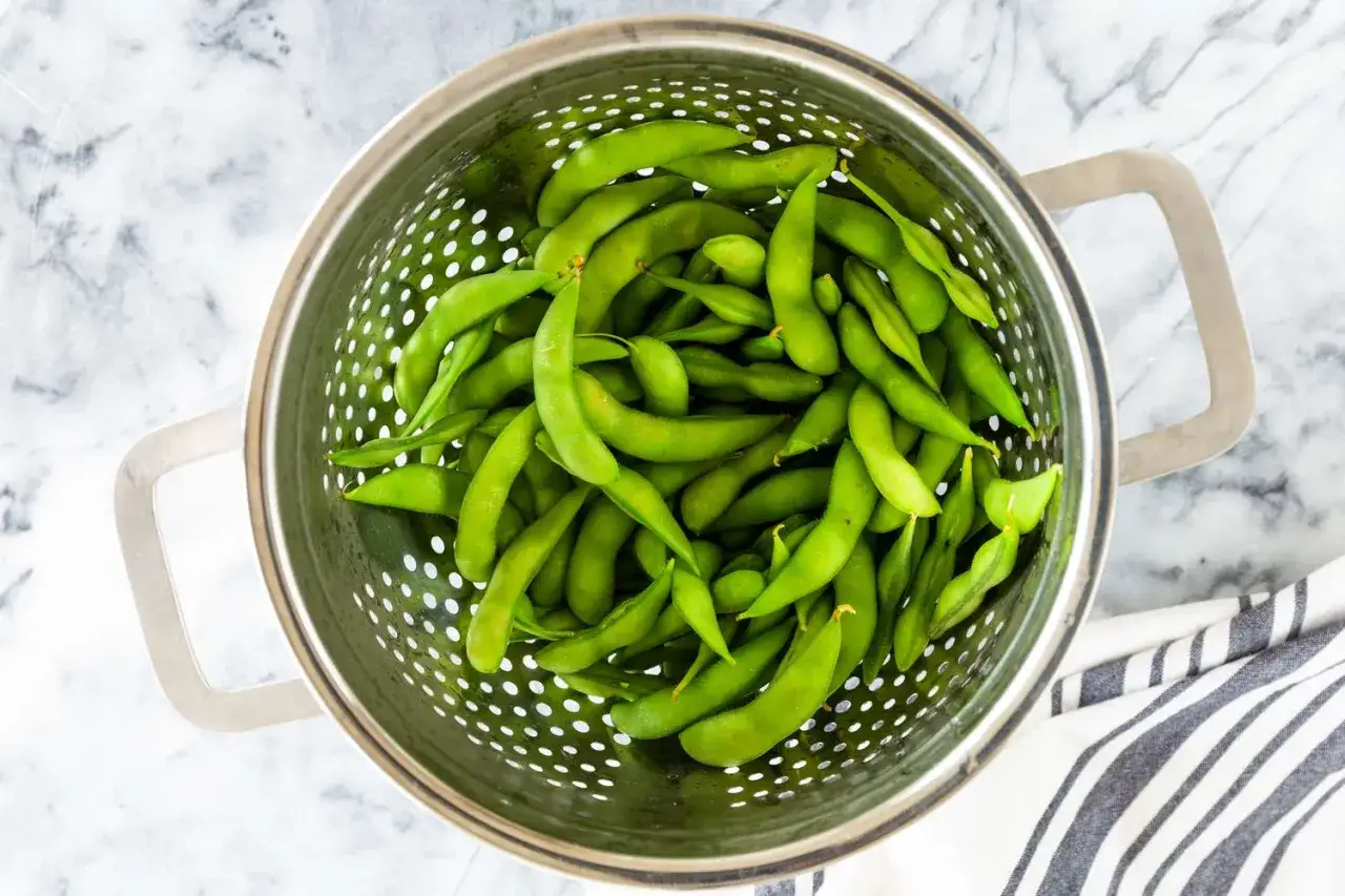 Świeże strąki fasolki edamame w durszlaku, gotowe do przygotowania według prostego przepisu.