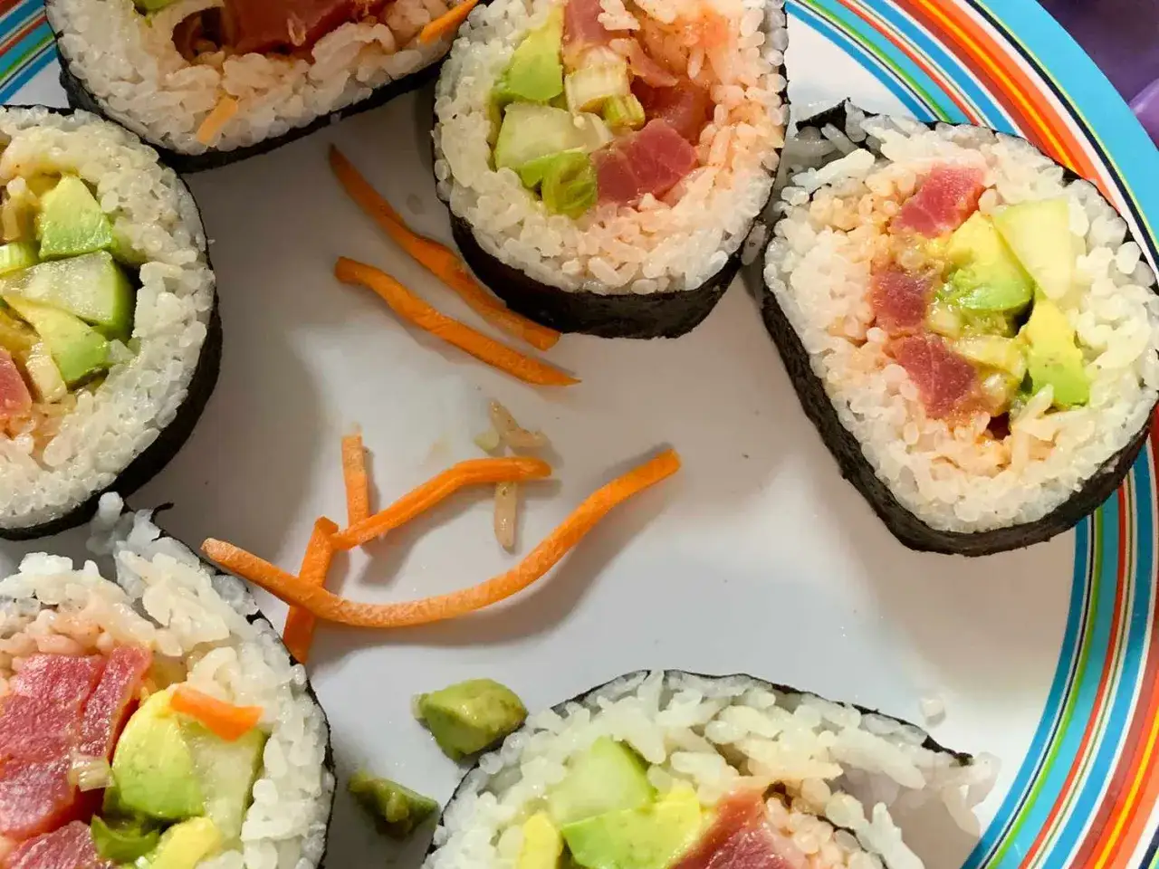 Roladki sushi z tuńczykiem i awokado, ozdobione startą marchewką. Idealne, gdy zastanawiasz się, jak przygotować tuńczyka do sushi.