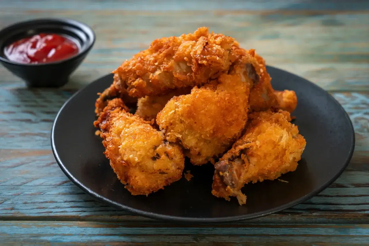 Chrupiące skrzydełka z airfryer na czarnym talerzu, obok miseczka z ketchupem. Idealne na przekąskę!