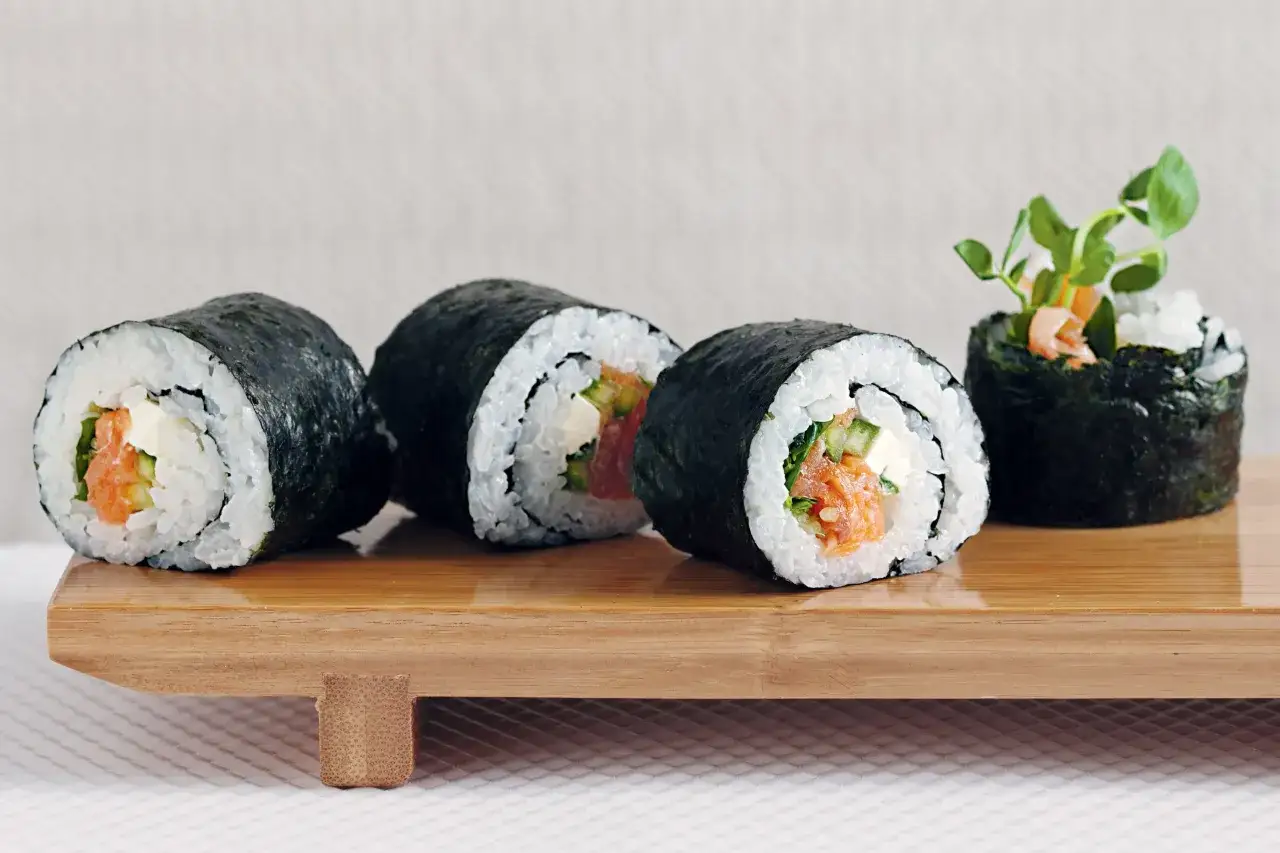 Roladki sushi z łososiem i kremowym serkiem, który jest idealny do sushi, na drewnianej desce.