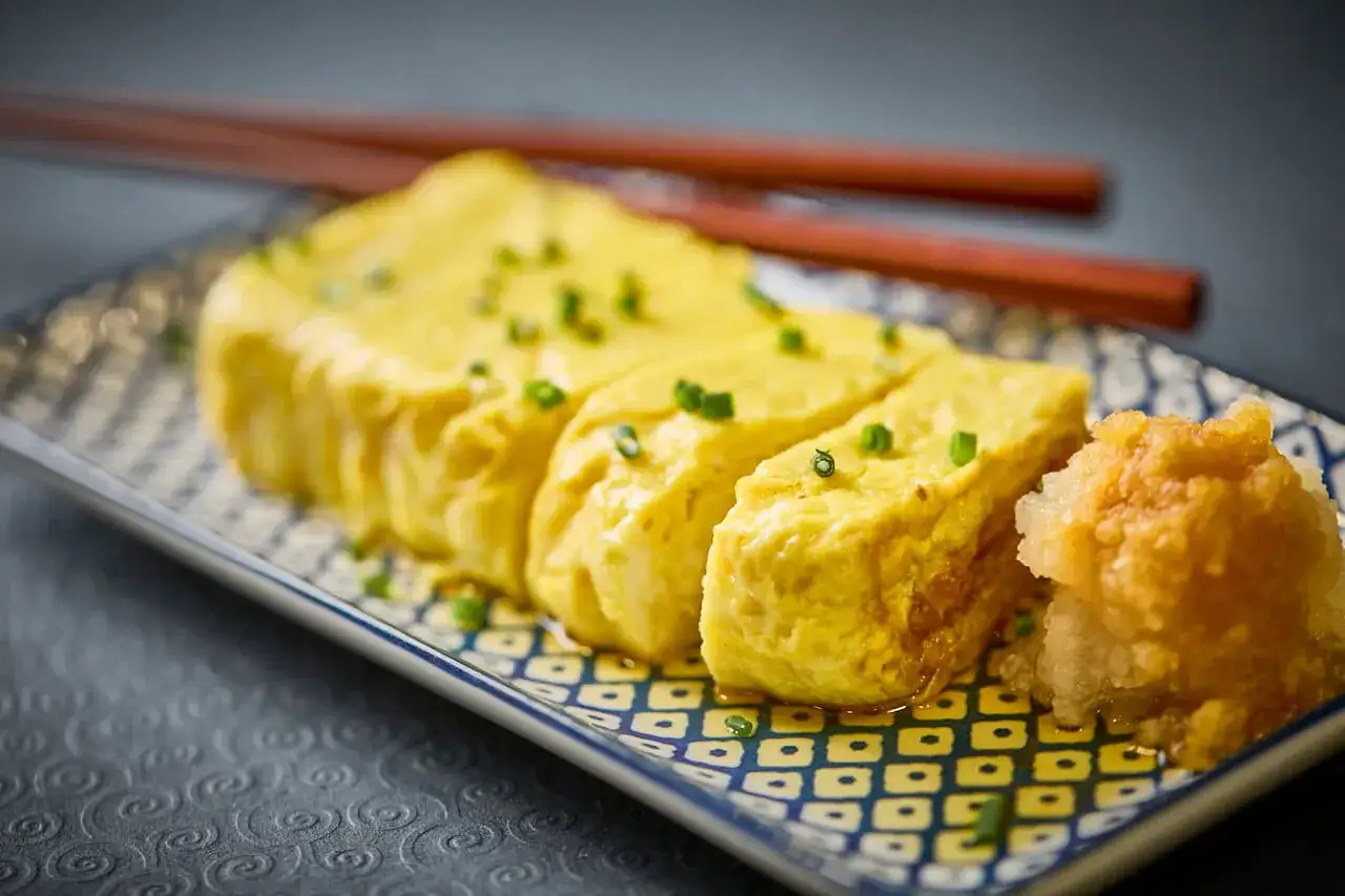 Delikatny omlet do sushi, pokrojony na kawałki i posypany szczypiorkiem, podany z tartą rzodkiewką.