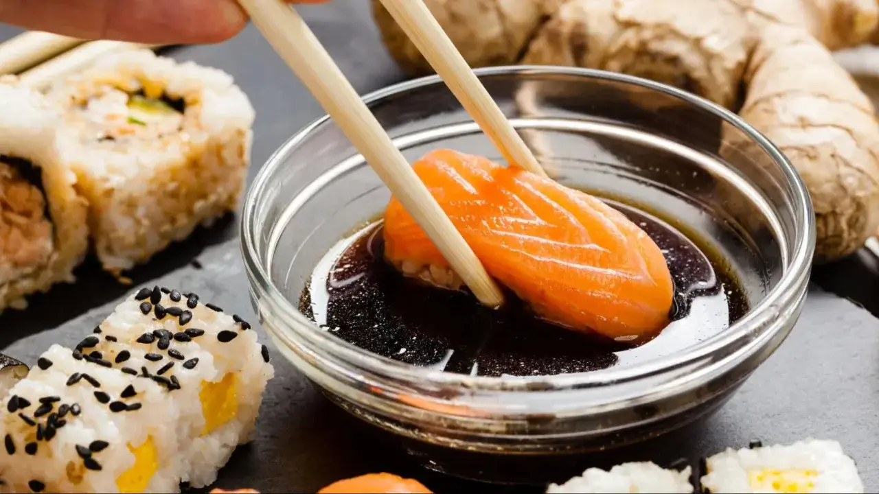 Łosoś zanurzany w sosie do sushi słodkim. Obok sushi z sezamem i imbir.