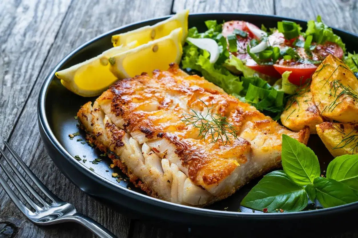 Idealny pomysł na rybę na obiad: soczysty filet rybny z chrupiącymi ziemniaczkami, świeżą sałatką i cytryną.